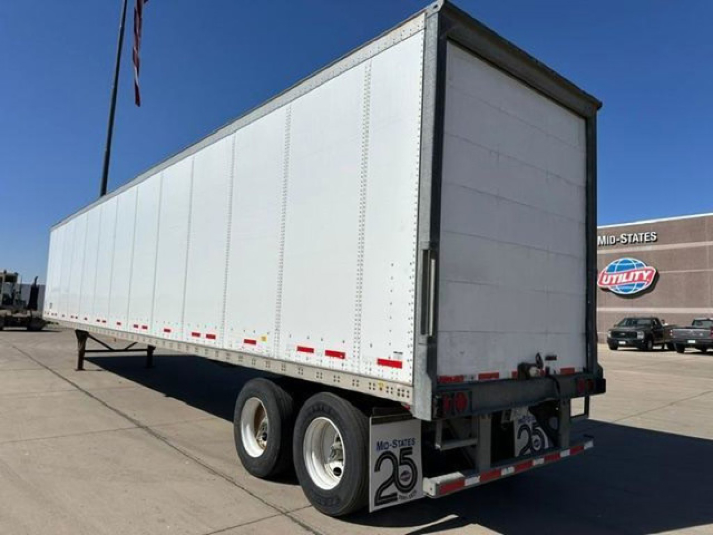 Trailer rear and side view showing long white box trailer with dual rear wheels and reflective tape.