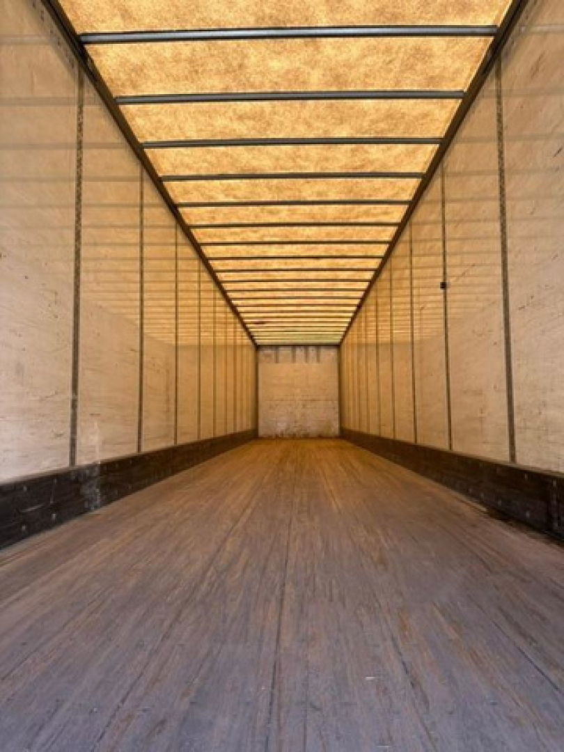 Interior of a long empty trailer with wooden plank ceiling and metal side walls; wooden floor with light and shadows.