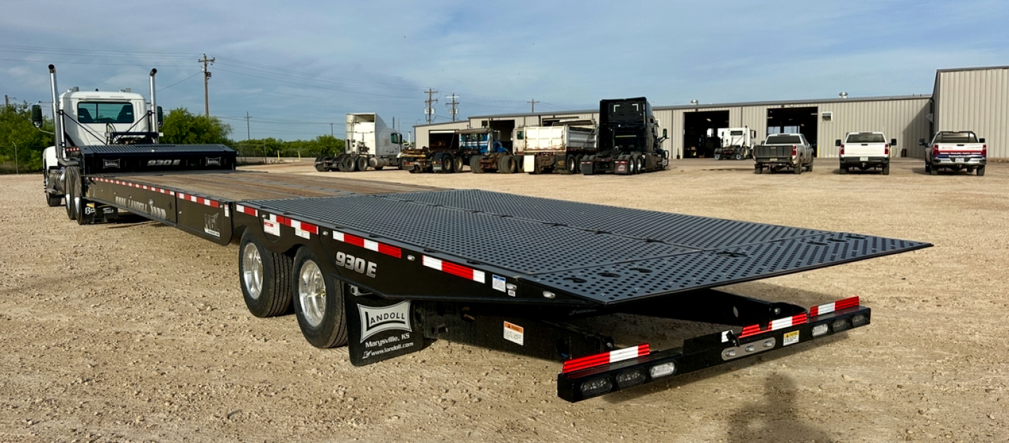 Flatbed trailer showing a long low-profile deck with a raised gooseneck and dual rear axles; 930E-51-15 model markings visible along the side.
