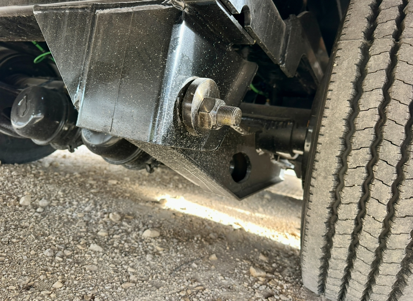 Truck trailer undercarriage showing thick bolt and frame bracket with wheel on right side.