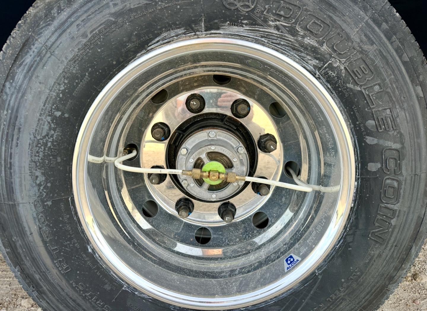 Wheel and tire of new trailer showing steel rim, lug nuts, central hub, and white nylon strap; visible brand text on tire sidewall.