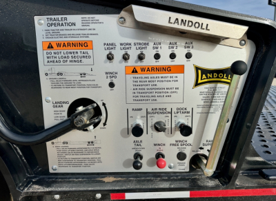 Landoll trailer control panel with labeled switches and warning decals. Panel shows 'LANDOLL' branding, multiple labeled switches (WINCH, AUX SW1-3, STROBE, AUX LIGHT), warning labels, and a ramp/axle control area.