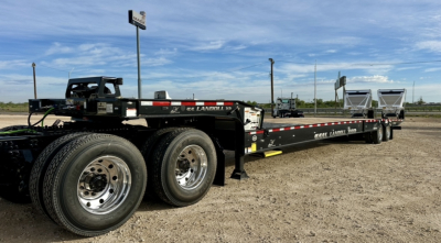 Landoll 930E-51-15 flatbed trailer showing dual rear axles, black deck, and white Landoll branding; long trailer with spare tire, round polished rims, and reflective safety tape along sides.