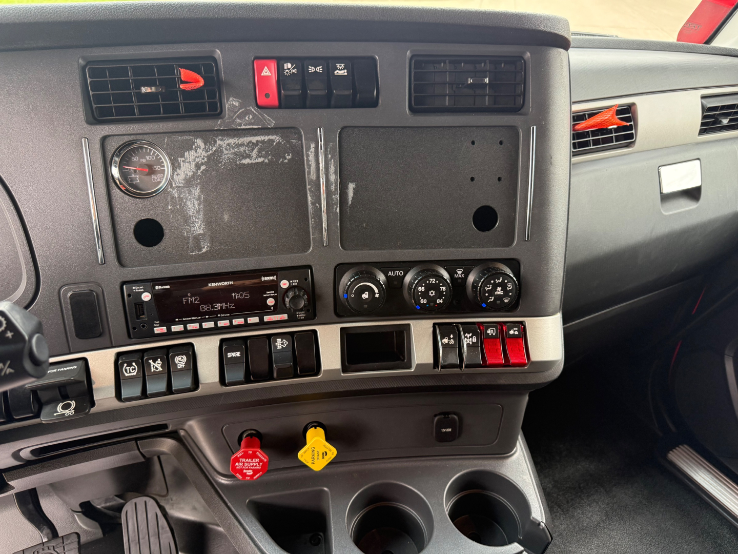 Cab interior dash cluster of a Kenworth T680 with multiple switches, gauges, and empty panels.