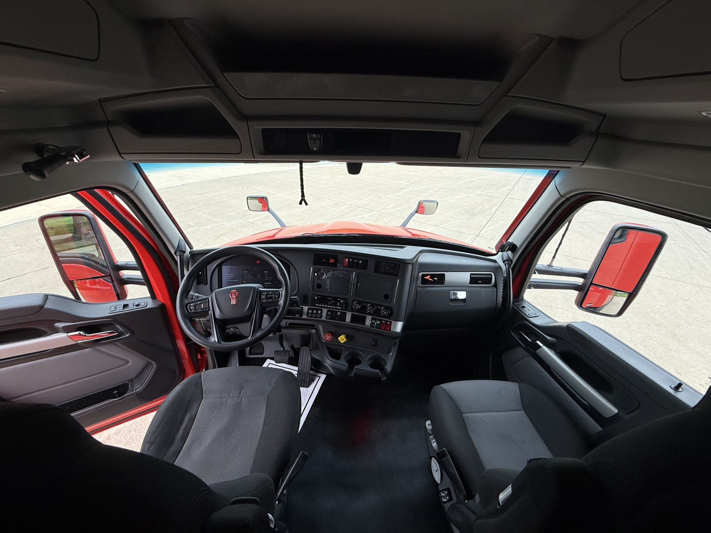 Kenworth T680 cab interior showing steering wheel, dashboard, and driver's seat with large side mirrors visible.