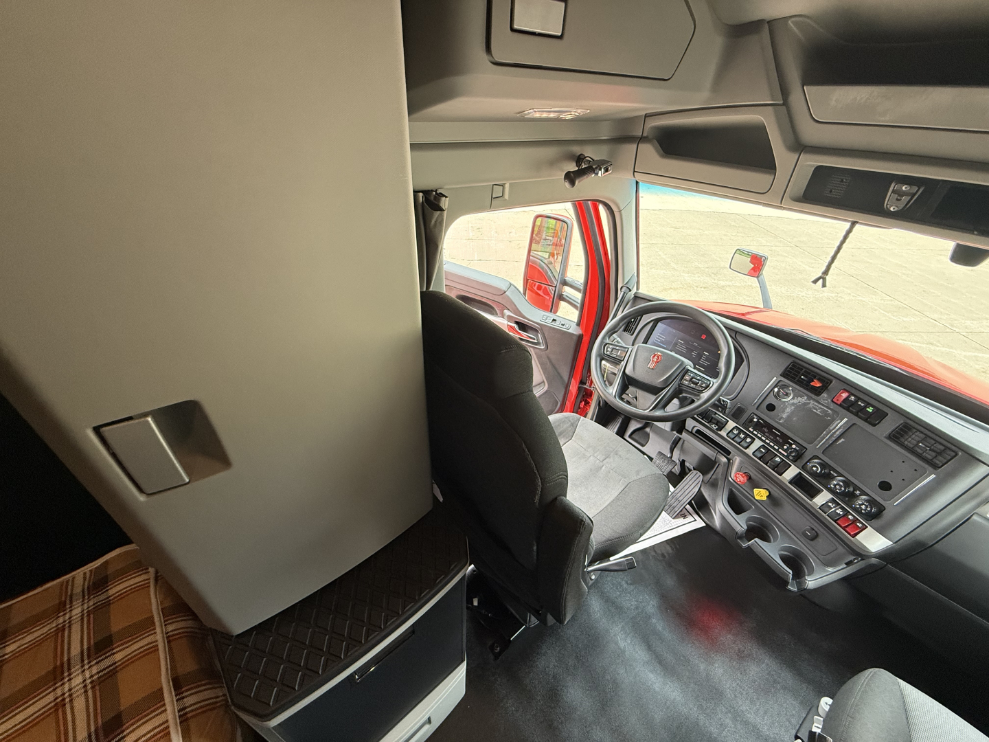 Kenworth T680 truck cab interior showing steering wheel and dashboard with sleeper area and storage cabinet
