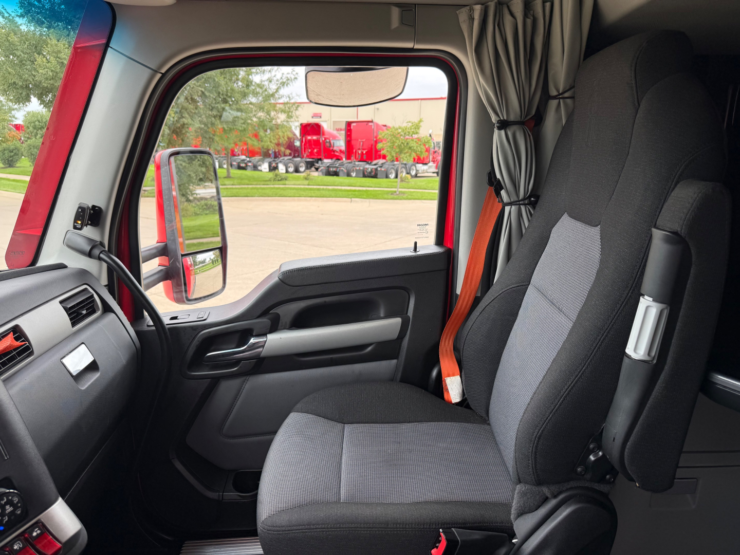 Truck cab interior front driver seat and window view of exterior parking lot; dashboard and door panel visible.