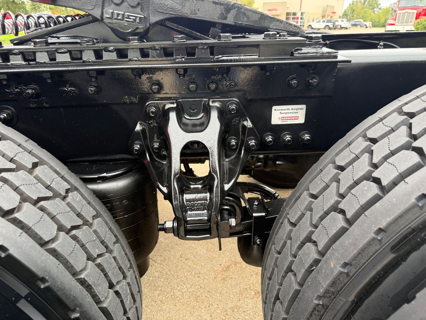 Kenworth T680 chassis undercarriage showing suspension components between dual rear wheels and mounting brackets; visible bolts and frame crossmember.