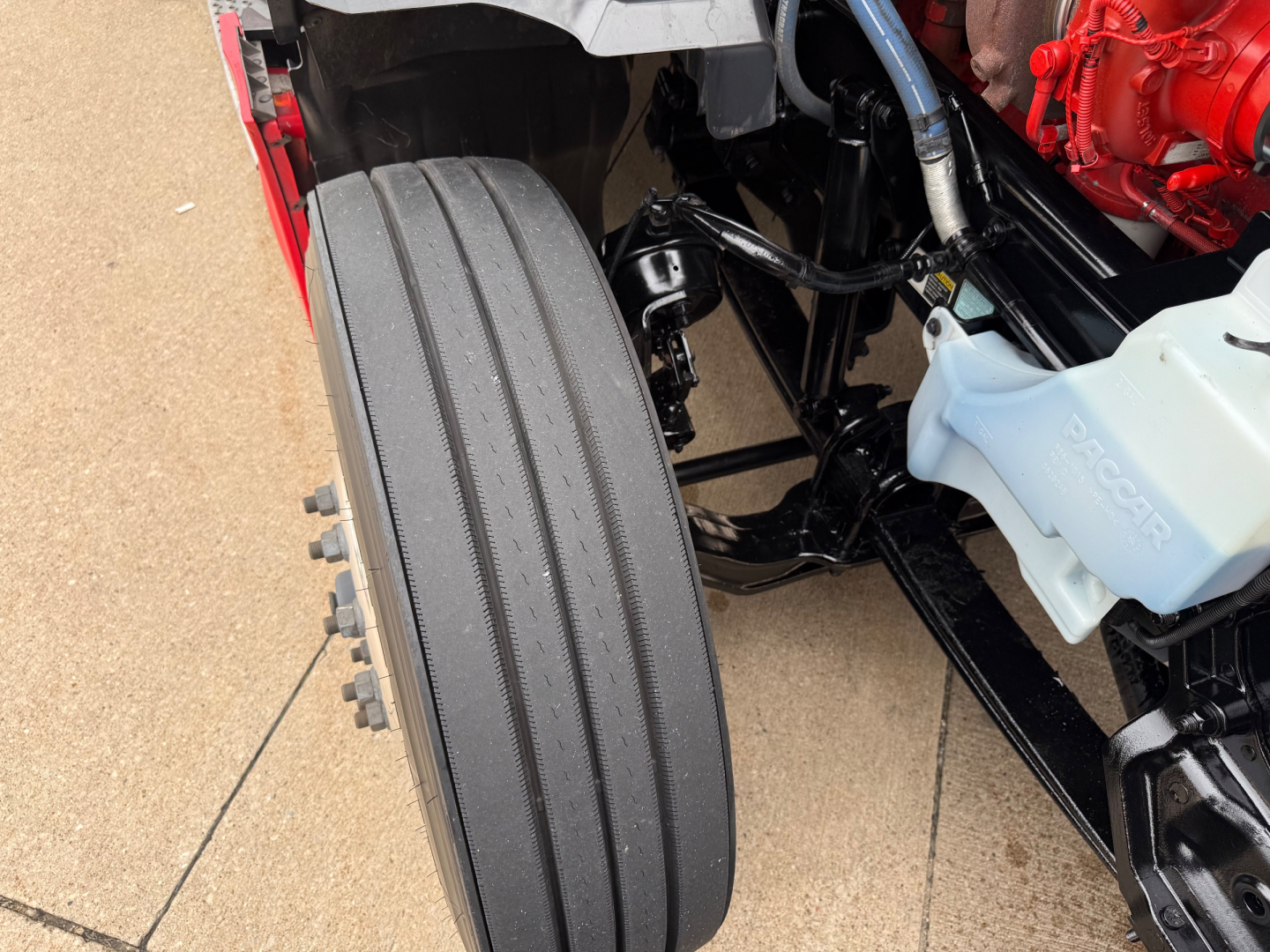 Kenworth T680 truck front axle and dual front tires, chassis and coolant reservoir visible in engine bay.