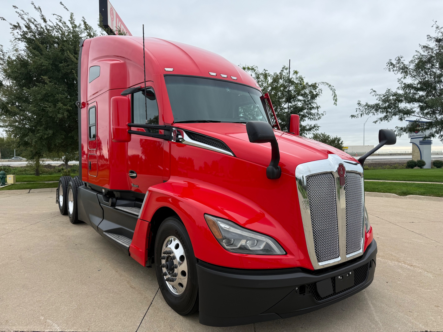 Kenworth T680 in red, front three-quarters view showing chrome grille, headlights, and side mirrors.