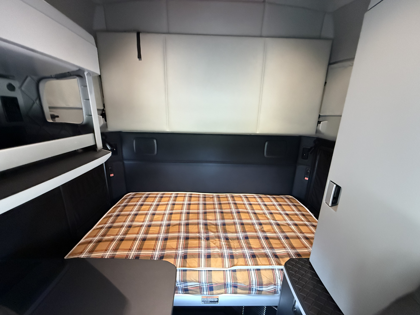 Kenworth T680 sleeper cab interior with plaid mattress in cargo area.