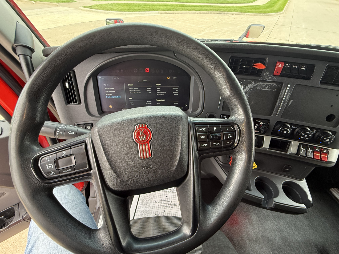 Kenworth T680 interior view showing steering wheel with logo, digital gauge cluster, and dashboard controls.