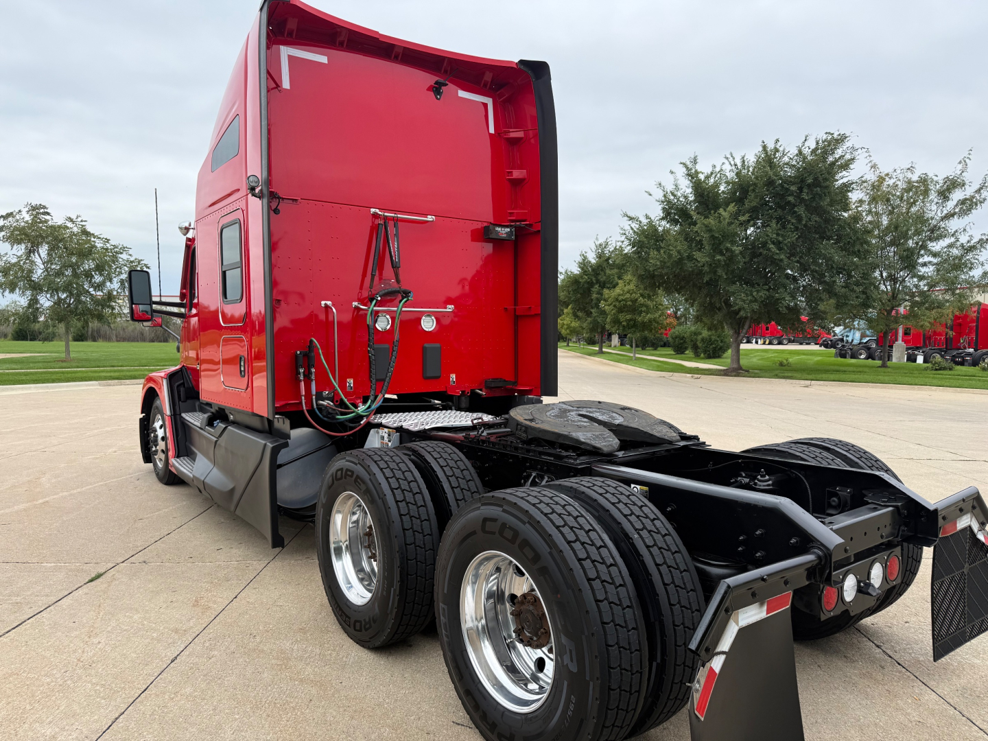 Kenworth T680 tractor cab rear with dual rear wheels, red exterior, visible fuel lines and chassis; fifth wheel area and rear lights.