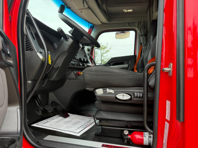 Cab interior of a red Kenworth T680 truck, focusing on the driver seat with controls, steering wheel, and dashboard visible through the open door.