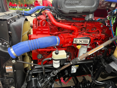 Kenworth T680 engine bay showing X15 badge, red engine components, blue hoses, coolant reservoir, and various hoses and wiring.