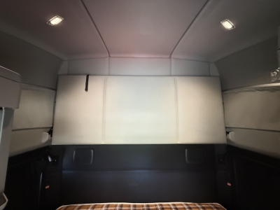 Kenworth T680 sleeper cab interior rear view showing light gray headliner and side panels with back of sleeper seat and storage pockets.