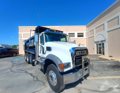 Mack GR84F dump truck shows front grille with Mack emblem and bumper guard, white cab, black dump bed, daytime exterior shot.