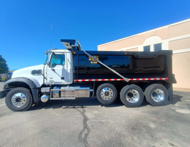 Mack GR84F dump truck side view showing large black dump body, chrome exhaust stacks, and dual rear wheel configuration with white cab.