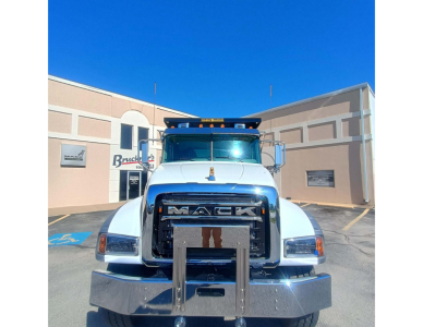 Truck front view showing Mack grille with bold MACK letters, chrome bumper, white cab, and blue sky; no readable model text beyond the brand name on grille.