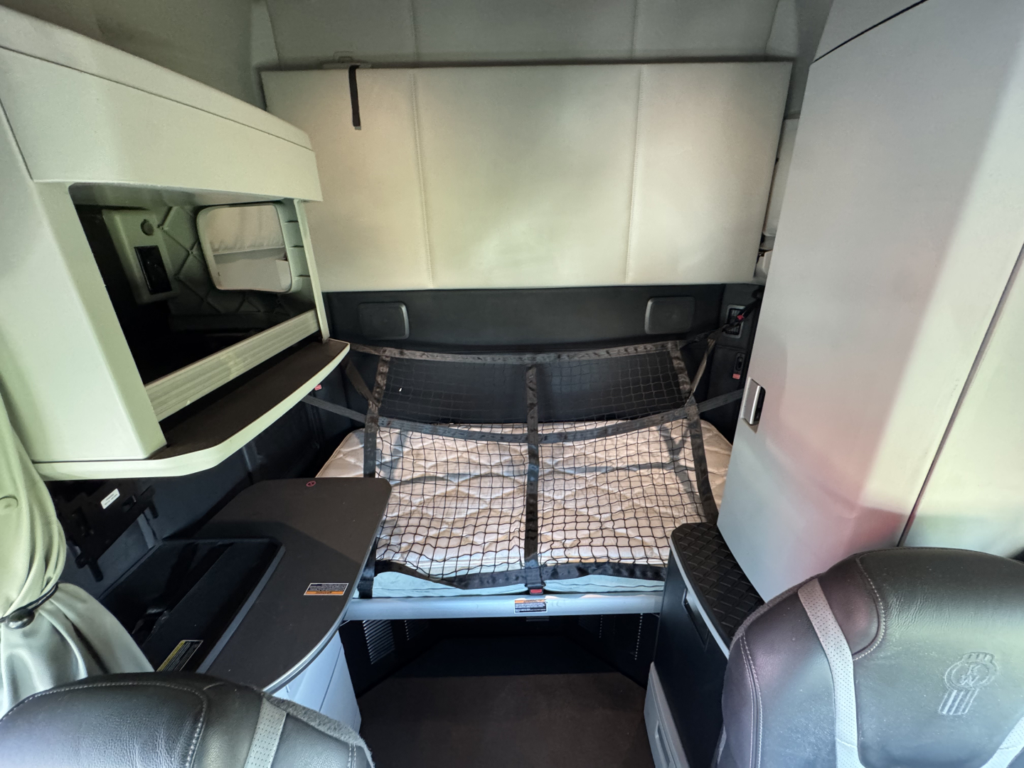 Kenworth T680 sleeper cab interior showing bunk bed with netting, storage compartments, and driver seat.