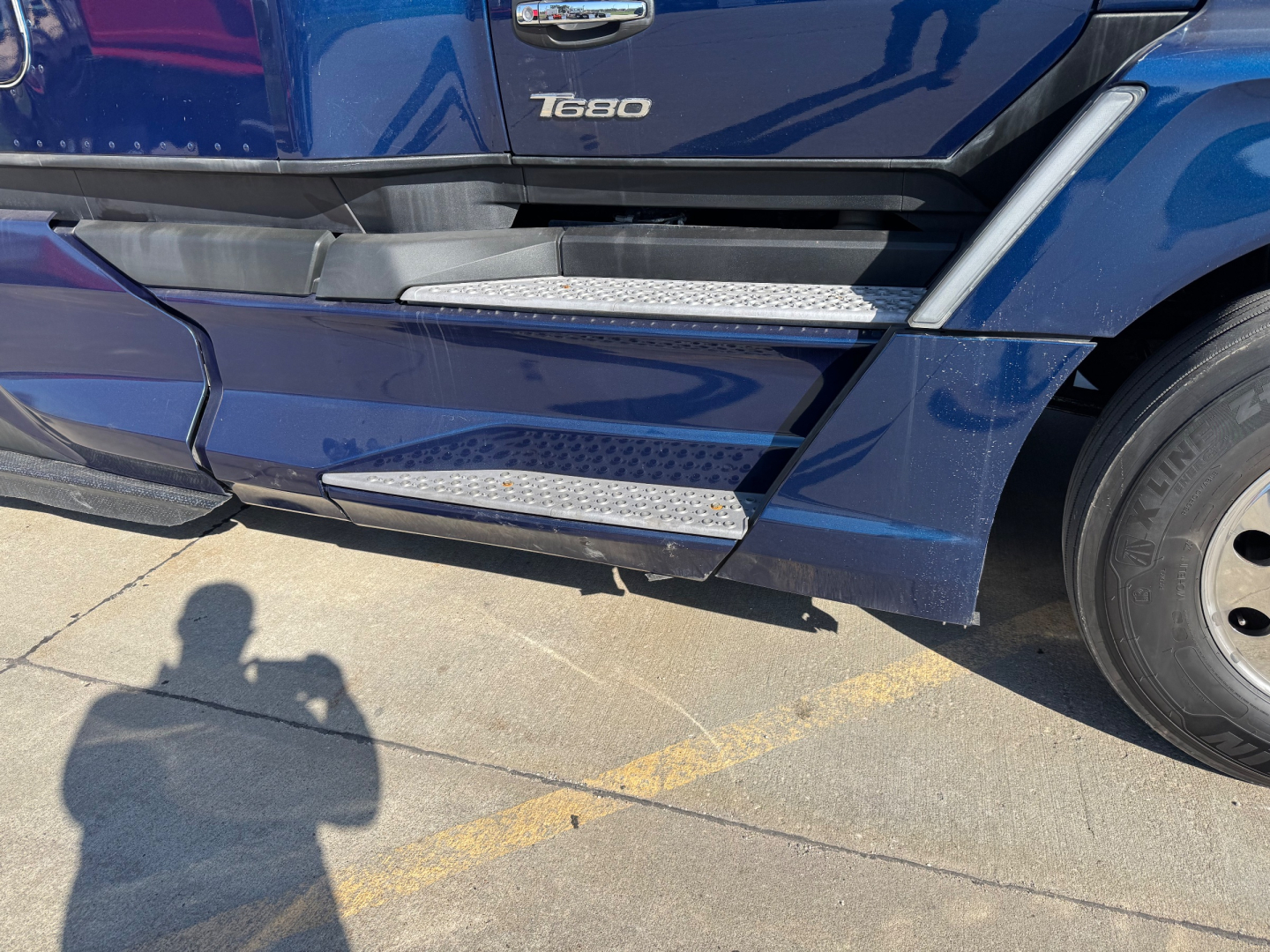 Kenworth T680 side view showing step boards and T680 badge on the cab, blue exterior, front wheel visible.