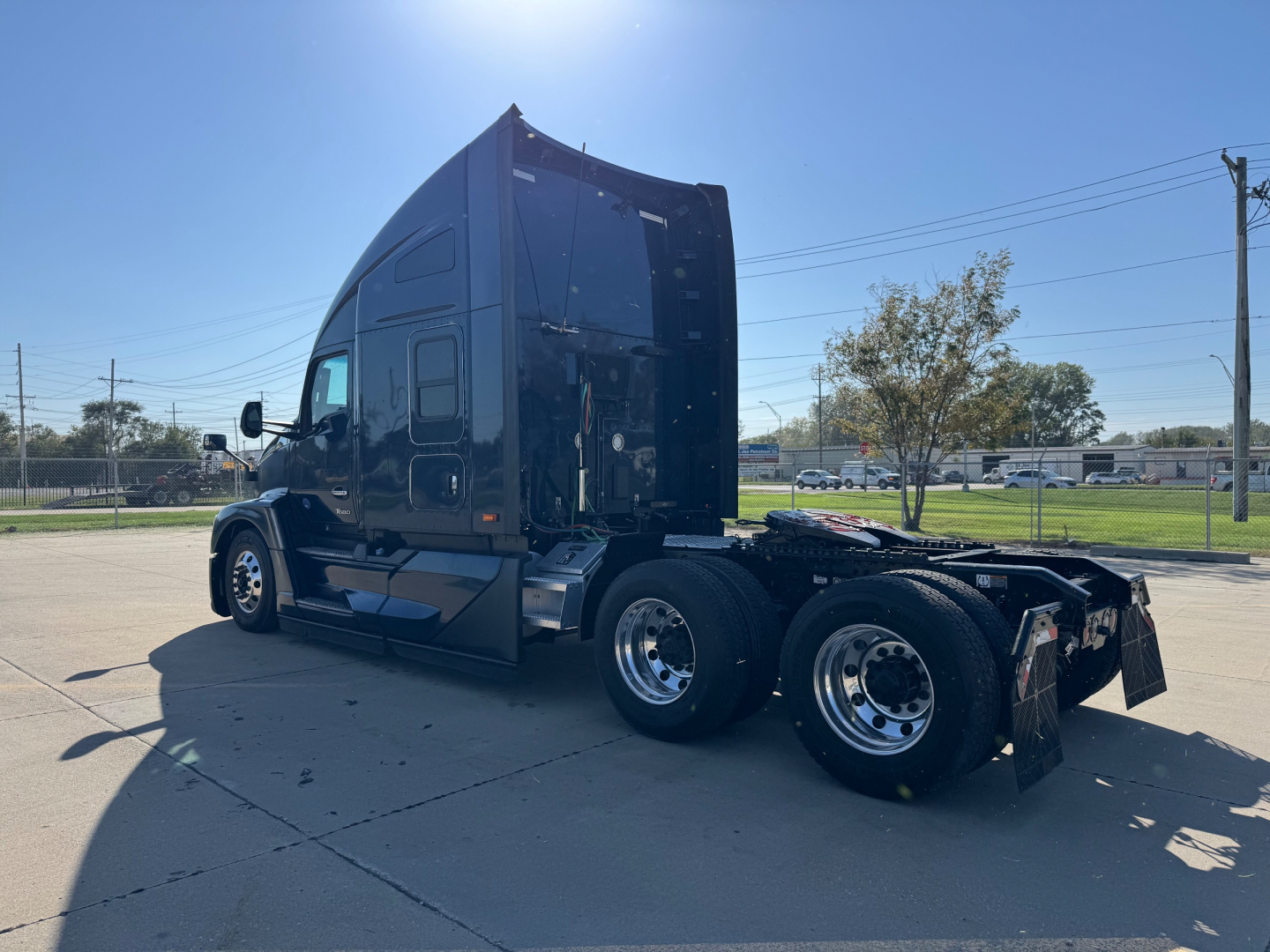 Kenworth T680 tractor from a side rear angle showing a black sleeper cab and dual rear axles on a parking lot.