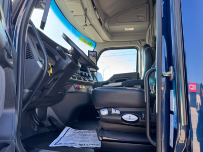 Kenworth T680 truck interior showing driver's seat, dashboard, steering wheel, and open door with blue exterior; visible controls and cabin shelving.