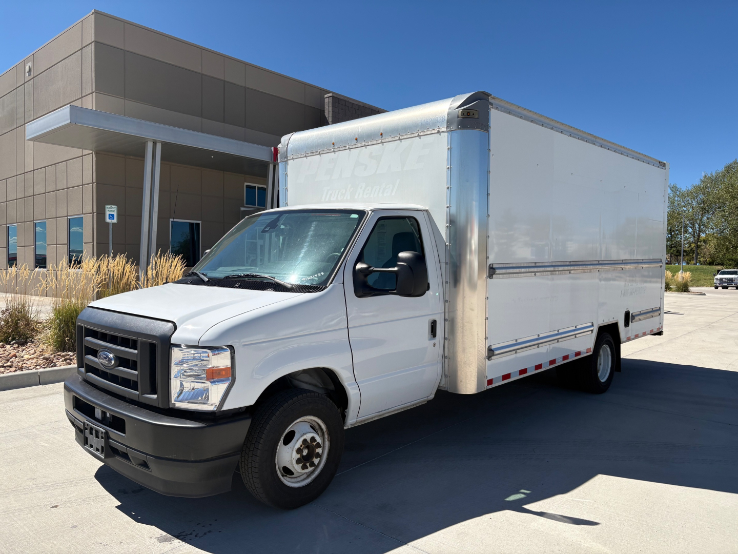 Ford E-350 box truck in front of building, white cab with rectangular box cargo area.