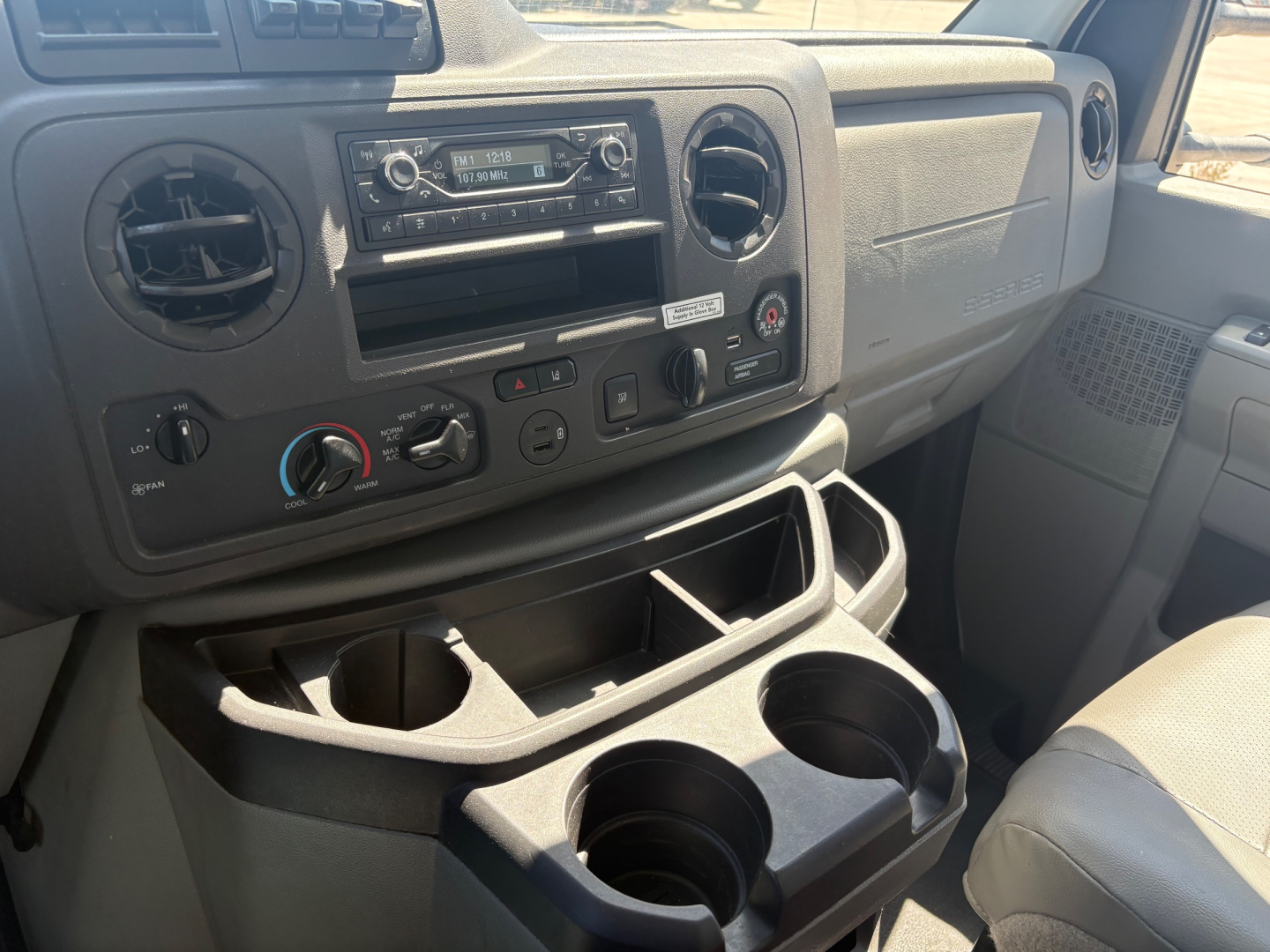 Ford E-350 cargo van interior dashboard with climate controls, radio, storage pockets, and cup holders in front cabin.
