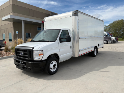 Ford E-350 box truck in front of a building, white cargo box, cab with black grille and bumper, side view shows dual rear wheels and long box.