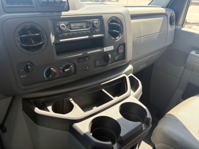 Ford E-350 cargo van interior dashboard with climate controls, radio, storage pockets, and cup holders in front cabin.