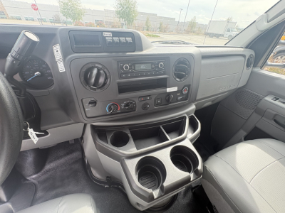 Dashboard of a 2022 Ford E350 cargo van interior showing center console with radio, climate controls, and cup holders. Visible text: nothing legible beyond typical controls.