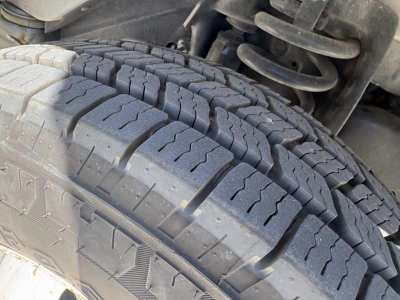 Ford E-Series van/box truck front wheel and suspension showing treaded tire with visible sidewall and coil spring in engine bay area.