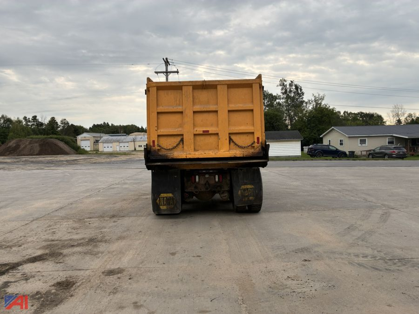 Dump truck bed of a yellow International dump truck viewed from rear; large hydraulic tailgate and heavy rear wheels visible.