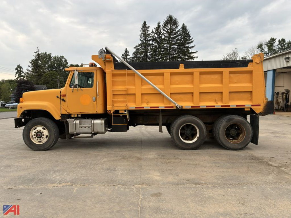 Dump truck side view showing orange 1995 International 2574 dump bed and hydraulic mechanism.