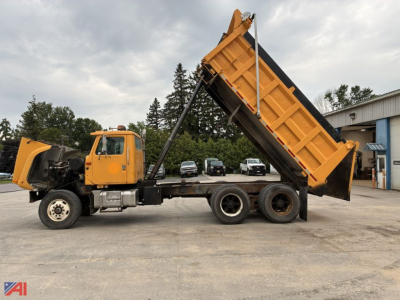Dump truck with raised dump bed on a three-axle chassis, yellow cab and bed, International 2574, side view showing hydraulic lift cylinder.