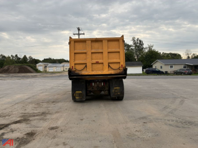 Dump truck bed of a yellow International dump truck viewed from rear; large hydraulic tailgate and heavy rear wheels visible.