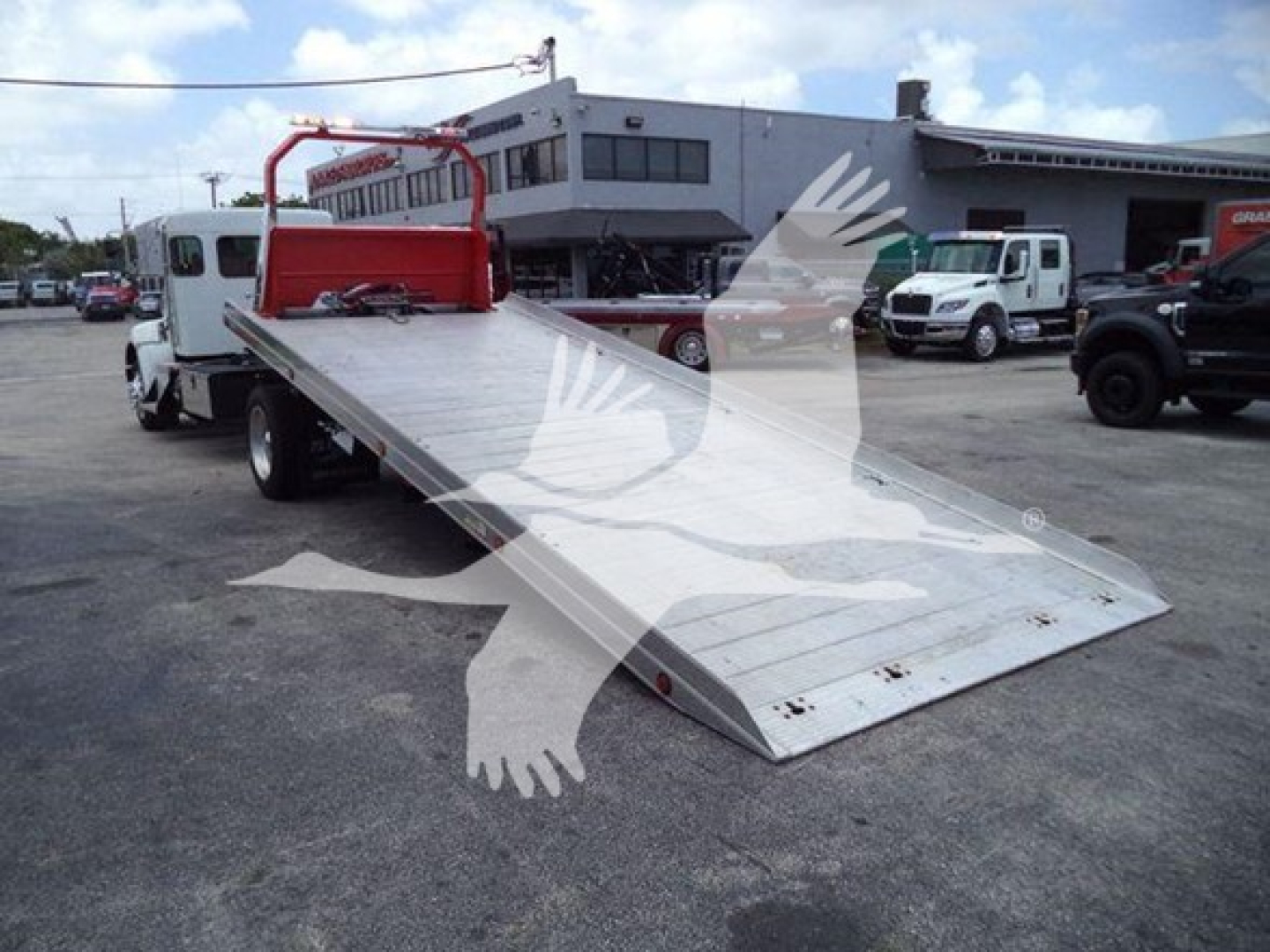 Flatbed tow truck bed on a 2019 Kenworth T270 rollback in a dealership lot, with a lower angled ramp and metallic surface.