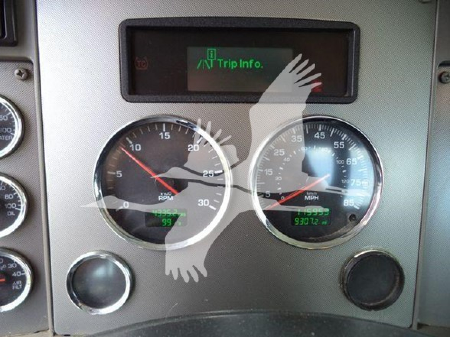 Dashboard of a Kenworth truck showing two round gauges and a digital trip info screen. Left gauge reads RPM with red needle, right gauge shows MPH, lower displays present mileage readouts.