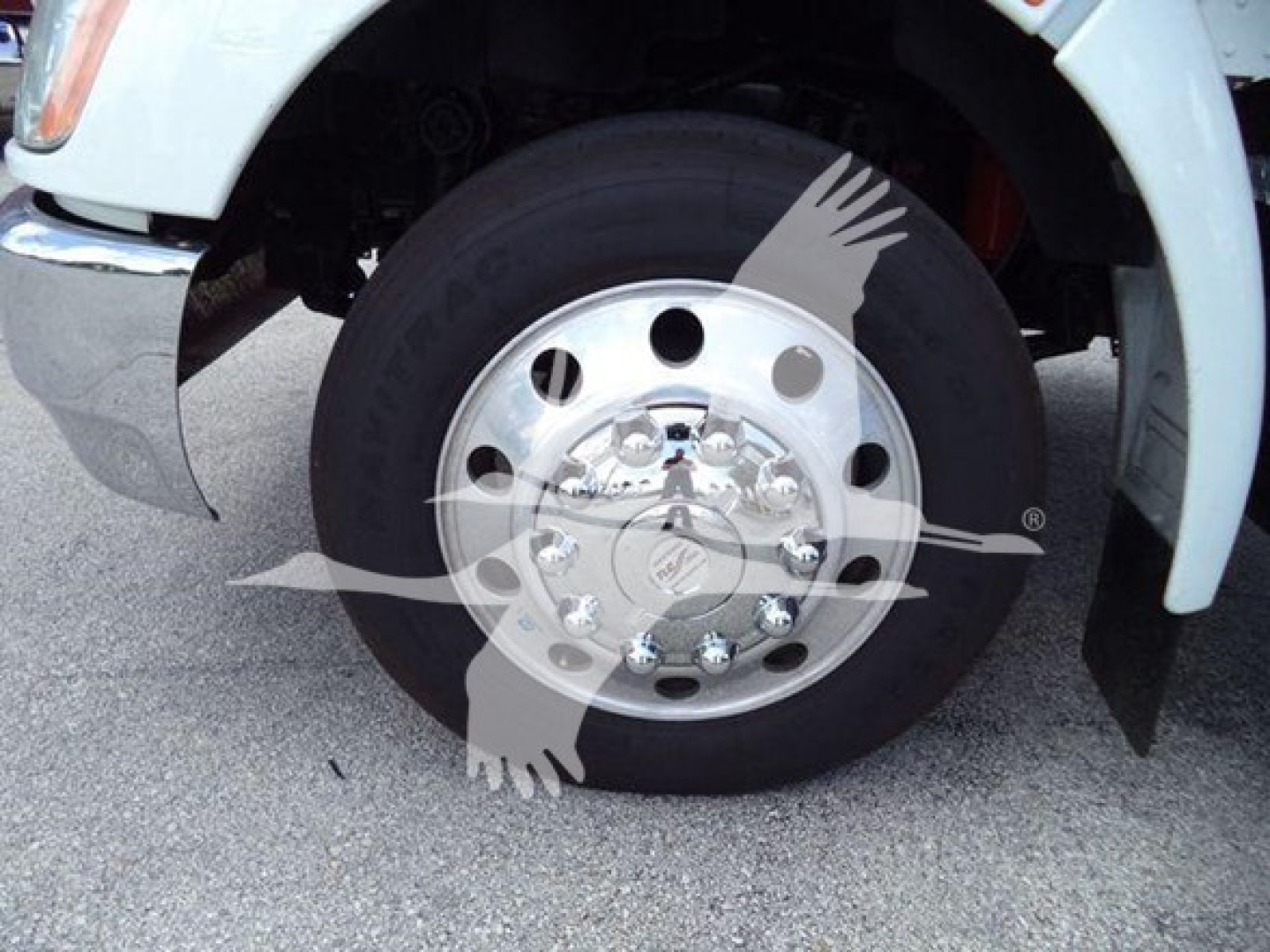 Kenworth truck wheel and tire close-up showing front axle with polished hub, lug nuts, and black tire; mudflap and white fender visible.