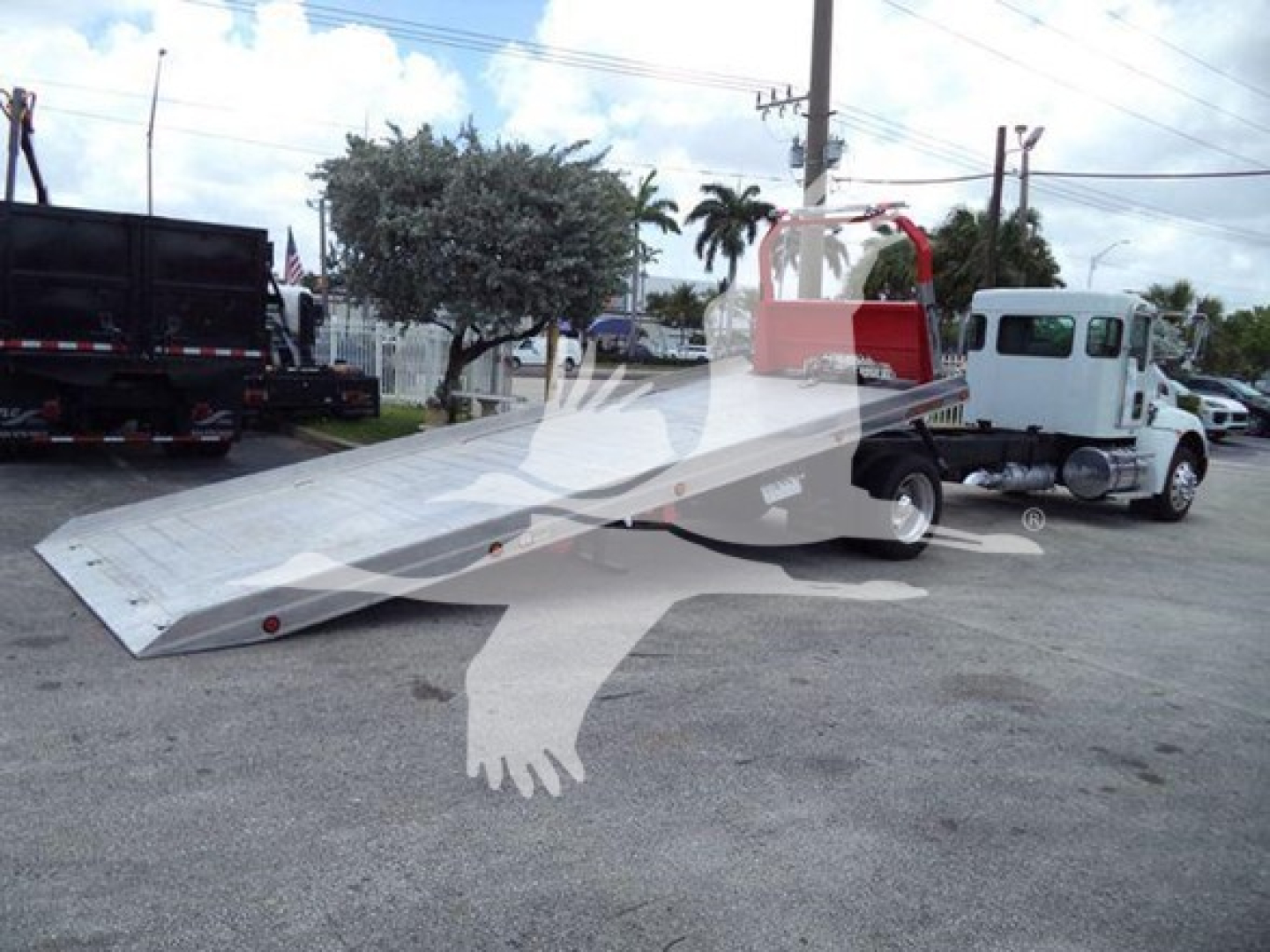 Kenworth T270 rollback truck with a long aluminum ramp bed, white cab, and red rollover protection arch. Foreground shows ramp extended on asphalt lot.