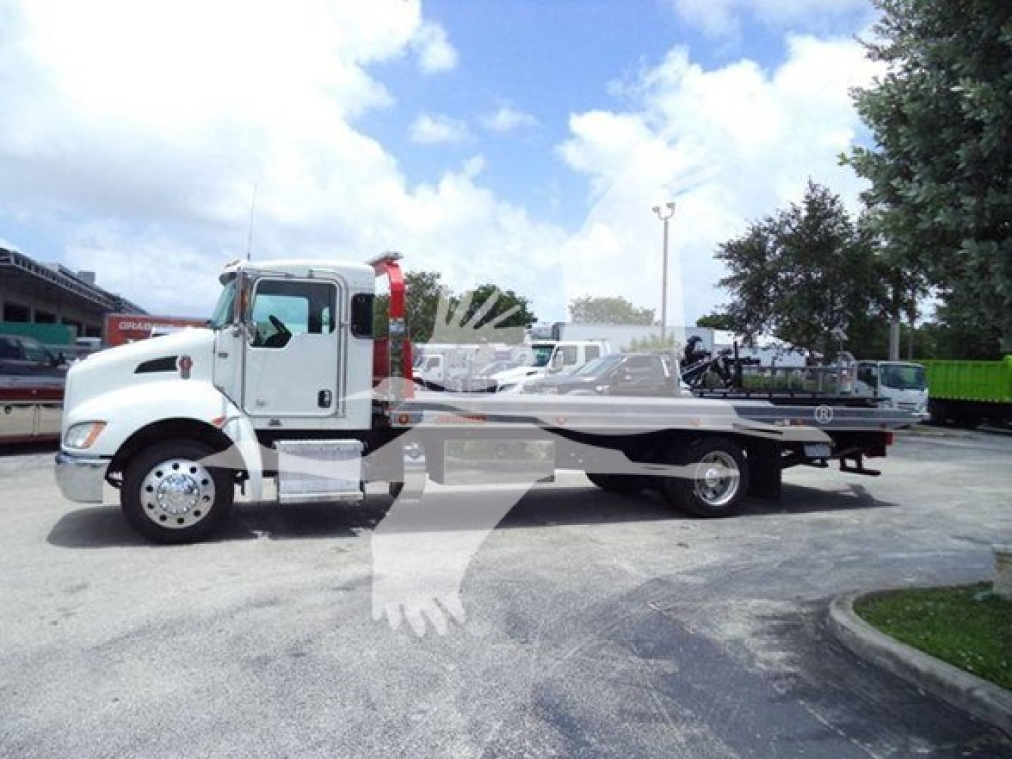 Kenworth T270 rollback truck side view with a long flatbed, white cab, and silver chassis in a dealership lot.