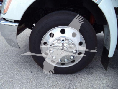 Kenworth truck wheel and tire close-up showing front axle with polished hub, lug nuts, and black tire; mudflap and white fender visible.