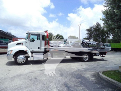 Kenworth T270 rollback truck side view with a long flatbed, white cab, and silver chassis in a dealership lot.