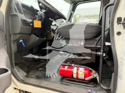 Truck cab interior showing driver seat, steering wheel, dashboard, and a red fire extinguisher on the cab floor near the door threshold.