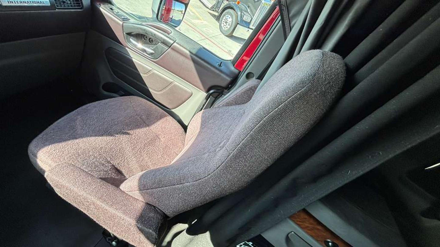Truck cab interior showing a gray fabric driver seat and door panel, with black curtains and wood trim accent.