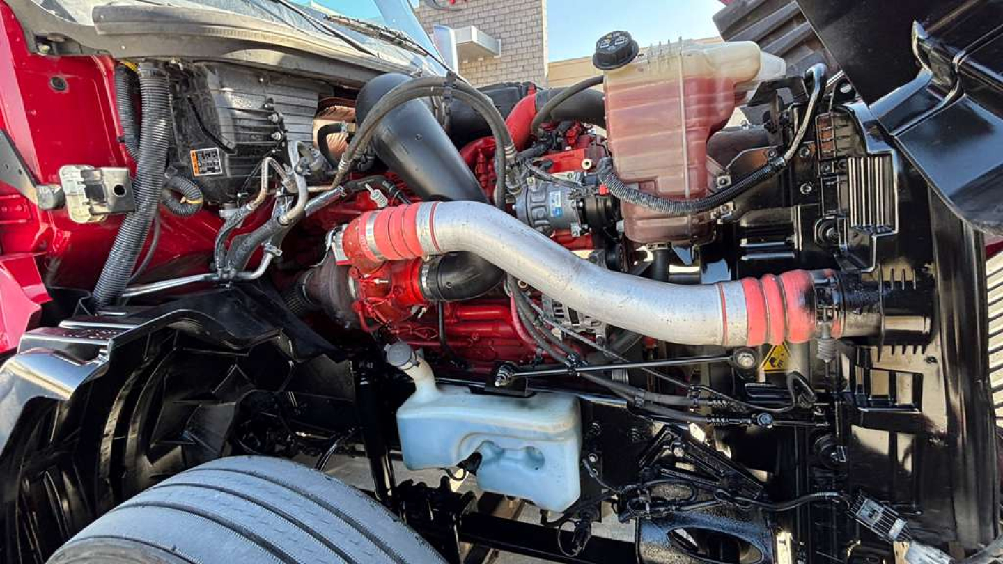 Engine bay of a 2022 International LT625 with red engine, silver exhaust, and various hoses; coolant reservoir and components visible.