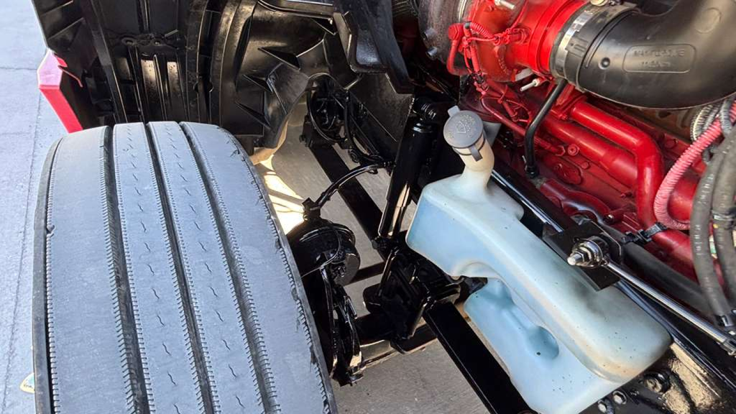Truck engine bay and front wheel area showing coolant reservoir and diesel engine components.