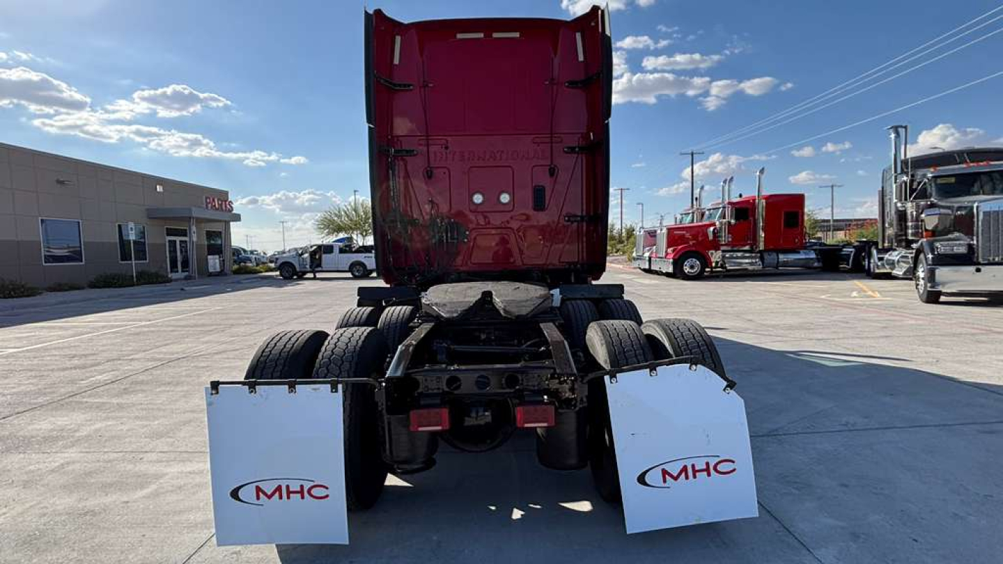 Truck rear view of a 2022 International LT625 sleeper cab showing rear dual axles, mud flaps with MHC logo, and red cab in the background.