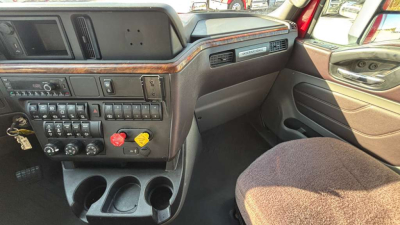 Truck cab interior showing dashboard controls, switches, and cupholders in driver area.